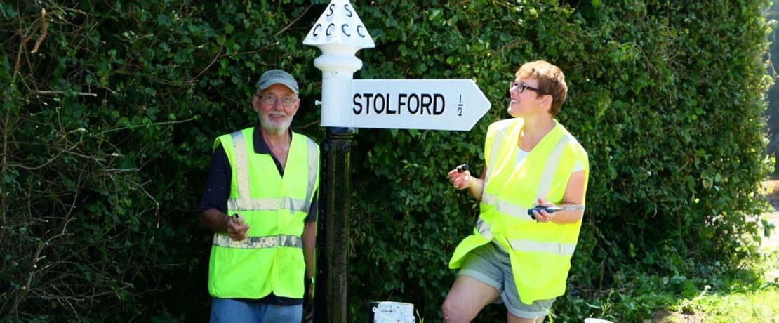 Two volunteers stand next to a newly painted fingerpost