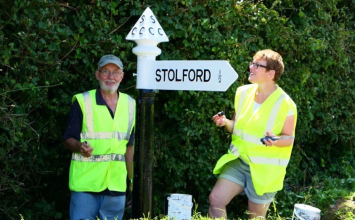 Two volunteers stand next to a newly painted fingerpost