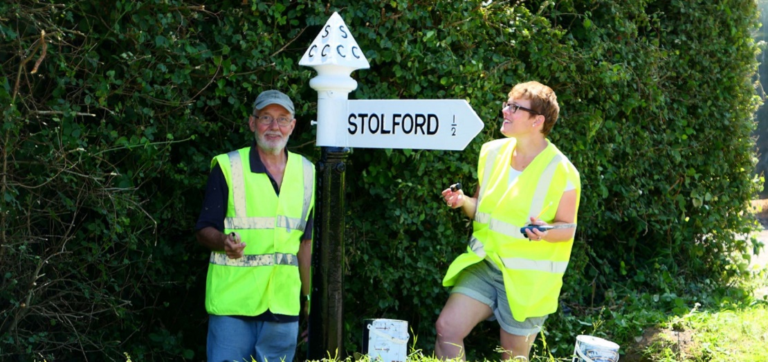 Two volunteers stand next to a newly painted fingerpost