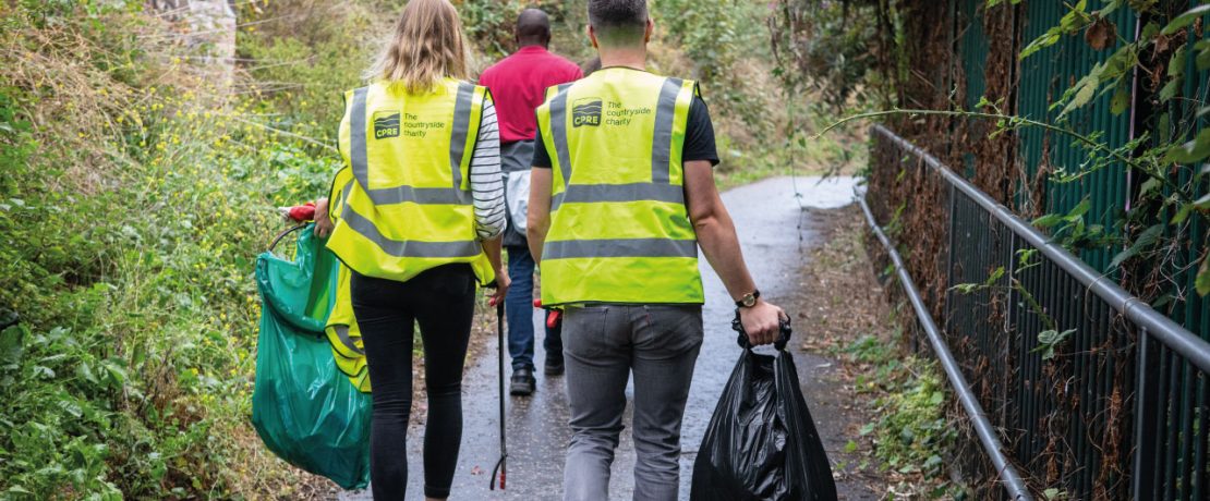 Two people walking in high-vis jackets with litterpicking gear