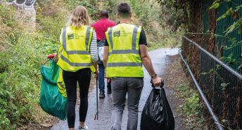 Two people walking in high-vis jackets with litterpicking gear