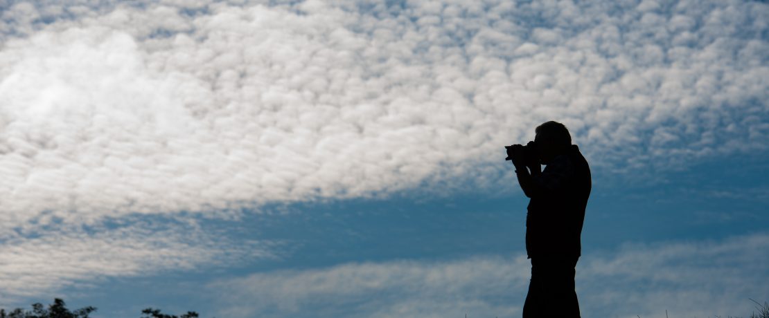 A man taking a photo with a cloudy sky