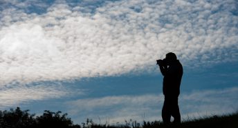 A man taking a photo with a cloudy sky