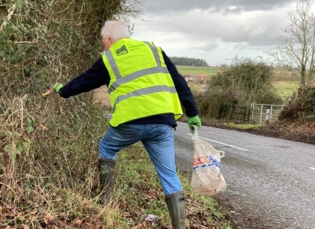 A man in a hi vis vest litterpicking on the roadside