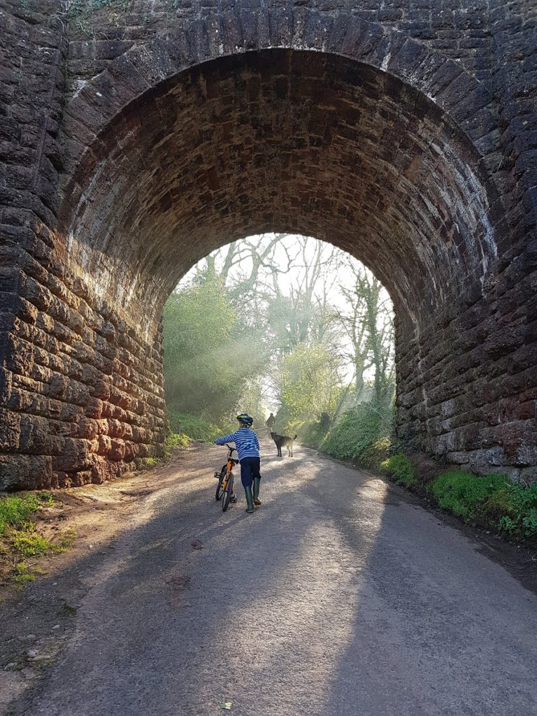 A child walks through a railway arch with a bike