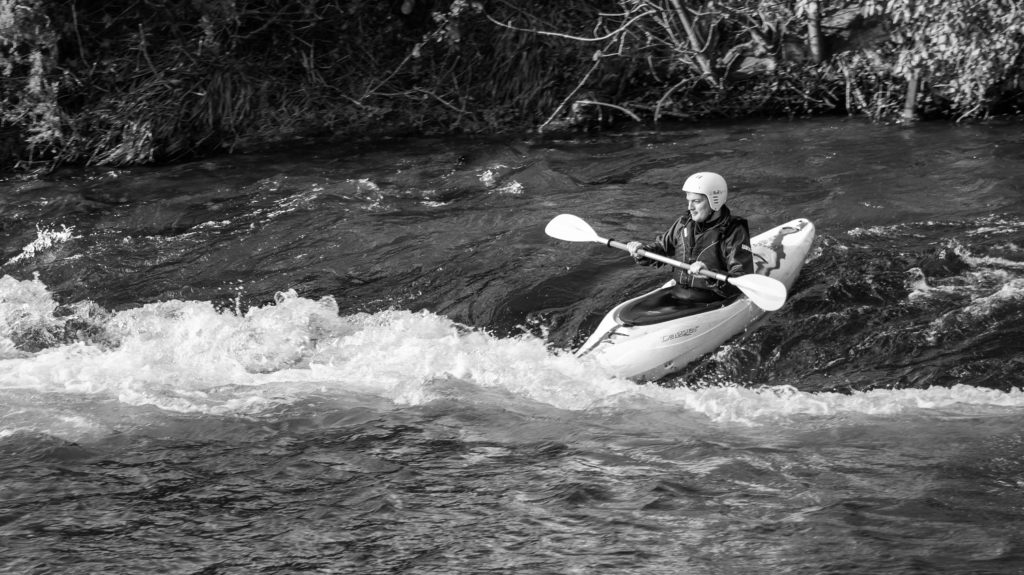 a black and white photo of a man canoeing a rapid