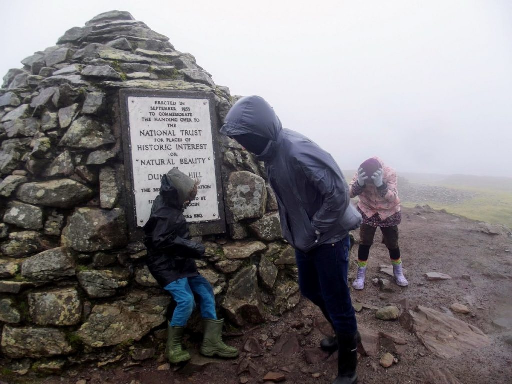 A family try and battle the wind on Dunkery Beacon