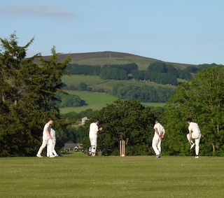 People playing cricket with a hill in the background