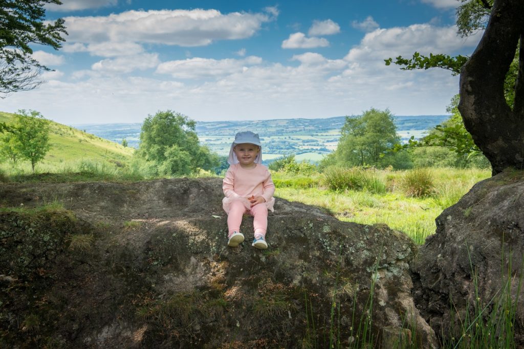 A child sits on a rock with countryside behind