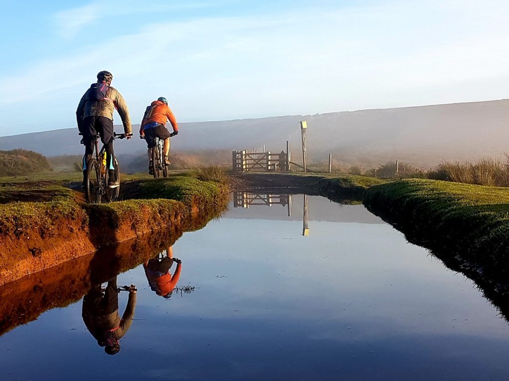 Two cyclists cycle next to a river