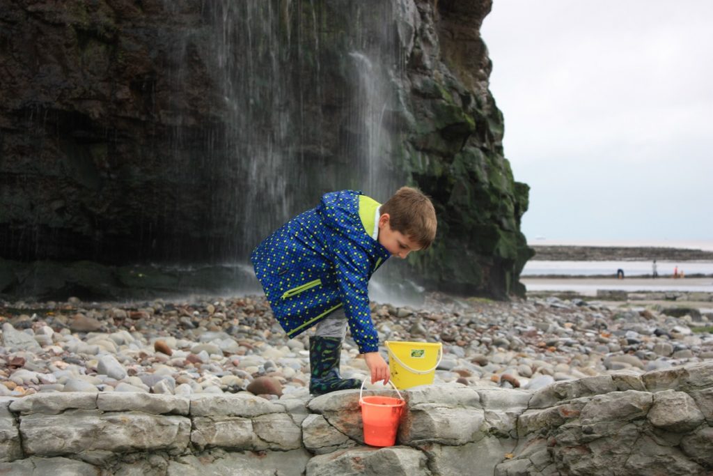 A child holds a bucket on a rocky beach
