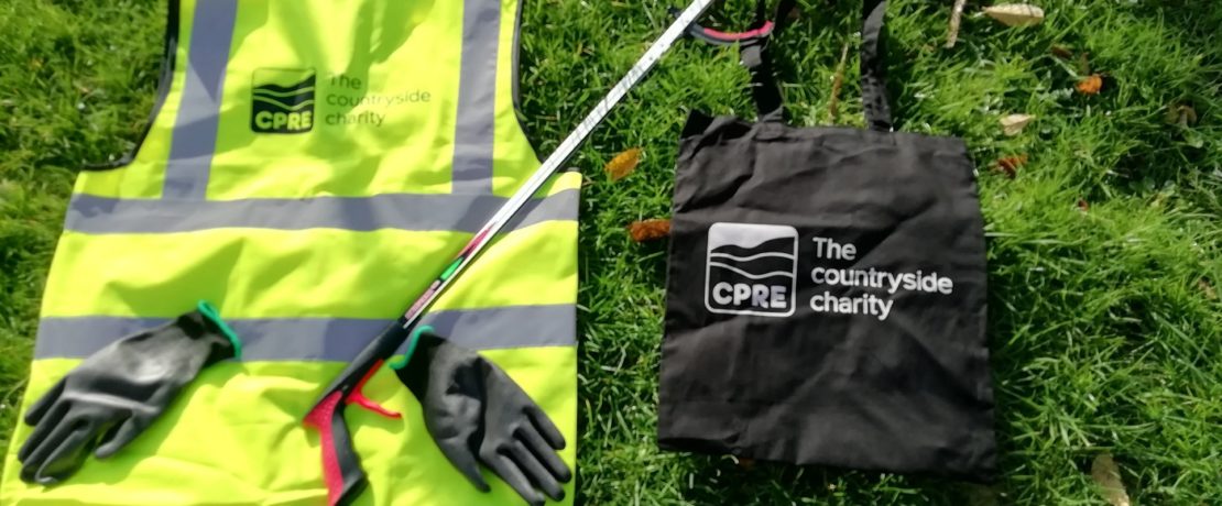 A hi-vis vest, a litterpicking stick, a pair of gloves and a branded bag laid out on grass