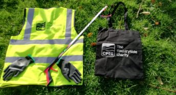 A hi-vis vest, a litterpicking stick, a pair of gloves and a branded bag laid out on grass