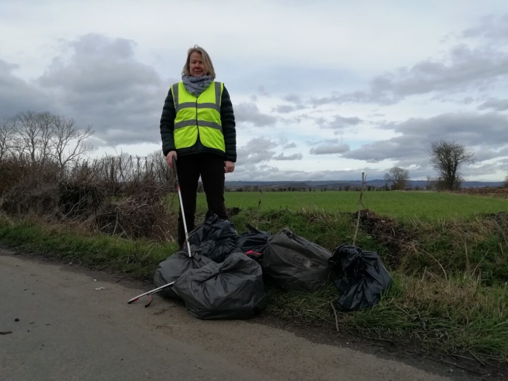 woman with bags of litter on a country lane