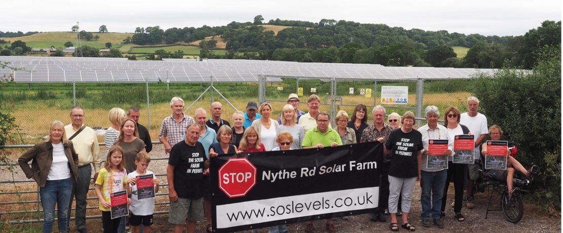 a group of people holding a banner in front of a solar farm