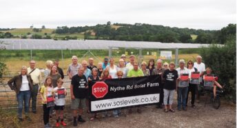 a group of people holding a banner in front of a solar farm