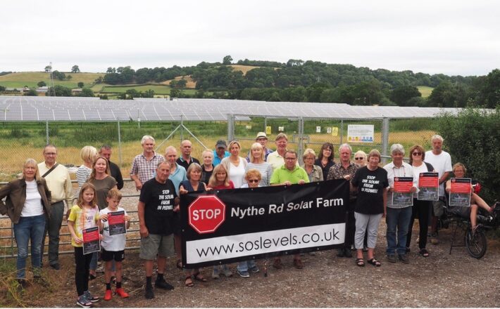 a group of people holding a banner in front of a solar farm