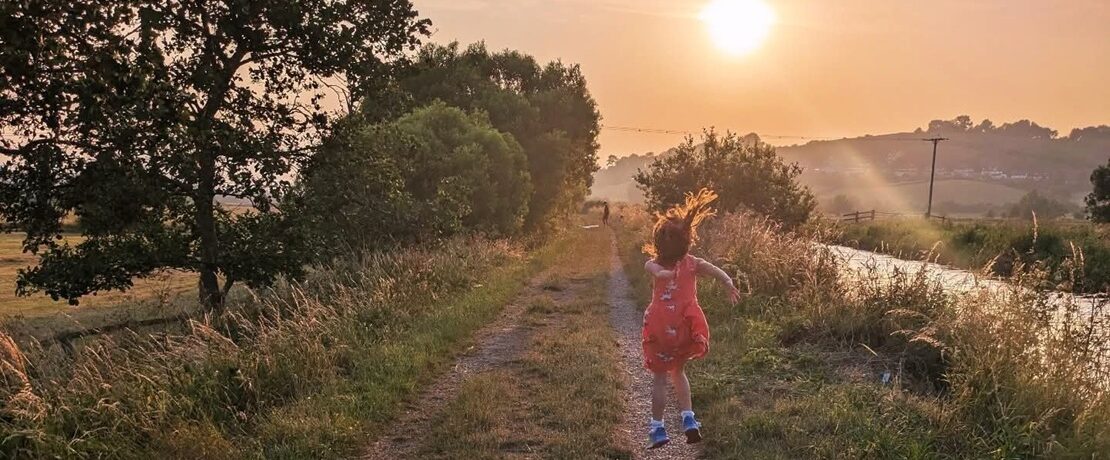 young girl jumping in the air by a riverside at sunset