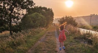 young girl jumping in the air by a riverside at sunset