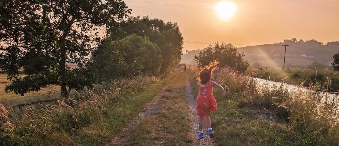 young girl jumping in the air by a riverside at sunset