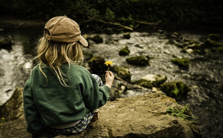 child looking at flower by stream